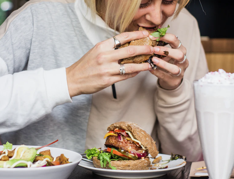 ハンバーガーを食べて血糖値が上がり太ってしまった女性のイメージ